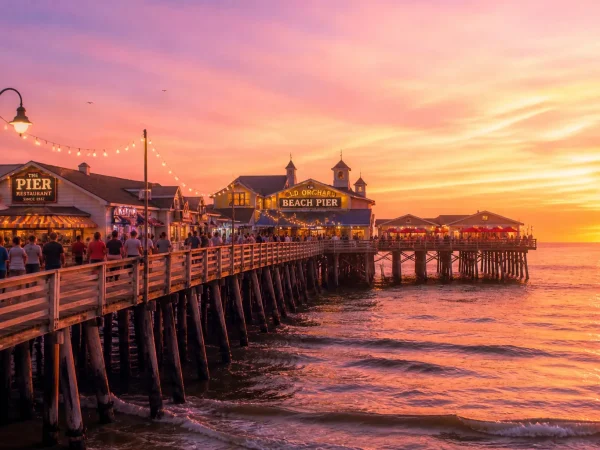 The historic wooden Old Orchard Beach Pier extending into the Atlantic Ocean at sunset with shops, restaurants, and warm summer light reflecting off the wooden boardwalk