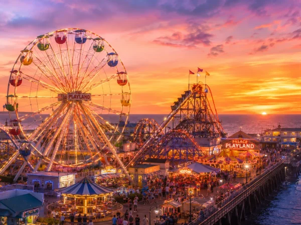 The colorful Ferris wheel and roller coaster at Palace Playland amusement park in Old Orchard Beach Maine glowing against a summer sunset sky over the Atlantic Ocean
